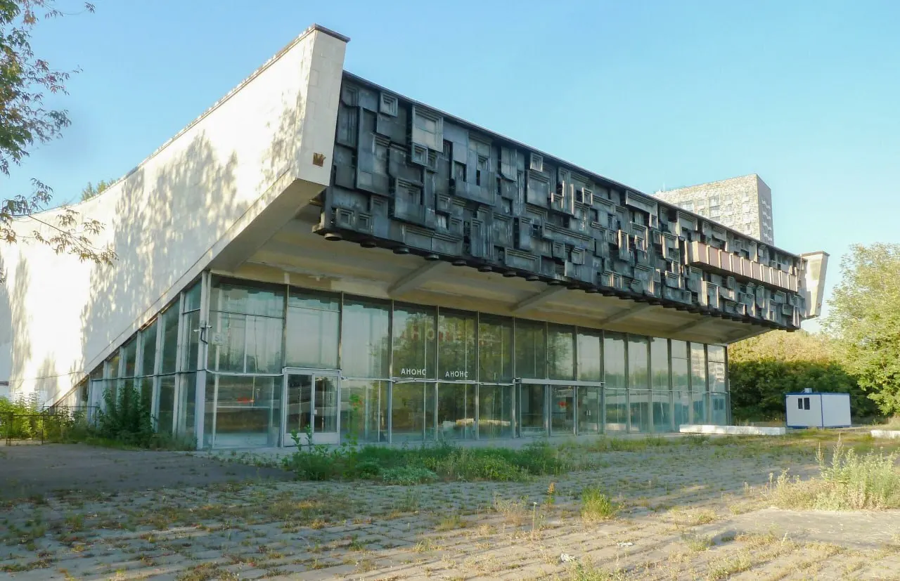 Заброшенный кинотеатр 1970-х с заметной скульптурной композицией простоял закрытым с 2005 года; его участок продали в 2013 году, а на месте здания планируют возвести почти 20 тыс. кв. м жилья.
